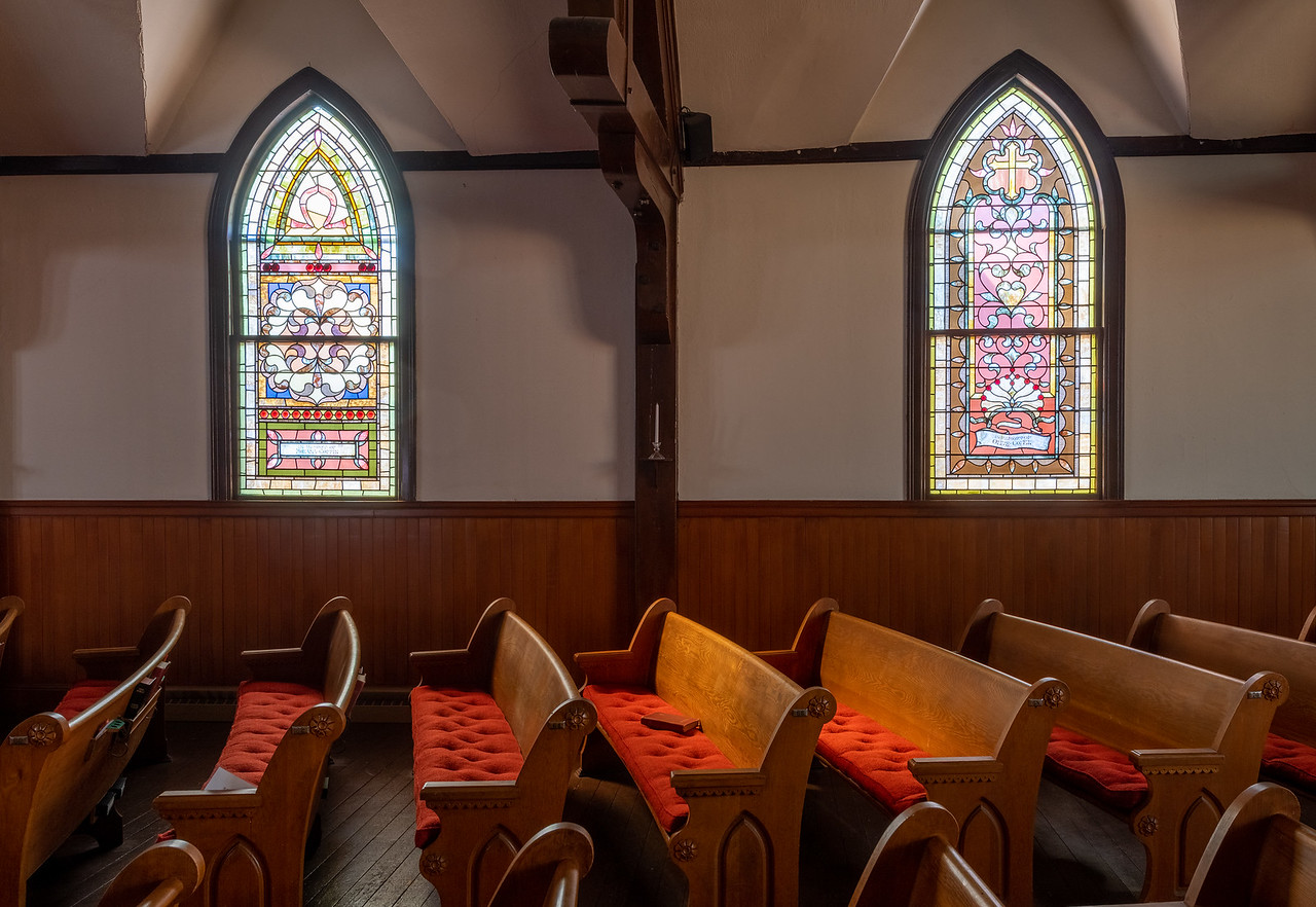 Church pews lit by sun through two arched stained glass windows